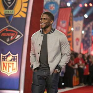 Reggie Bush, casually dressed, at a sports awards ceremony. Vibrant background with team logos