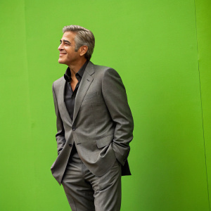 George Clooney in a candid photo. Gray suit, no tie. Vibrant green background