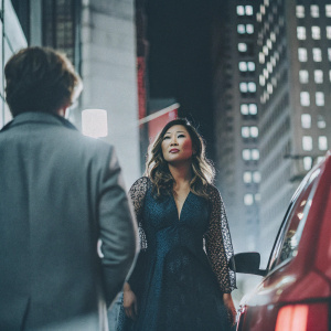 Jenna Ushkowitz, Asian actress, gracing the cover of People magazine. Wearing an elegant royal blue dress with intricate mesh overlay. Standing amidst a bustling cityscape at night.