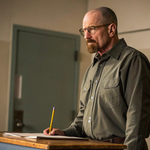 Walter White from Breaking Bad, wearing glasses and a beard, looking intense. Next to him is a desk with a pencil.