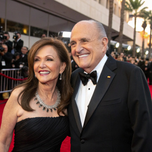 Judith Nathan and Rudy Giuliani at a Hollywood gala. Both are formally dressed, smiling broadly. The background is a bustling red carpet event with paparazzi and fans.