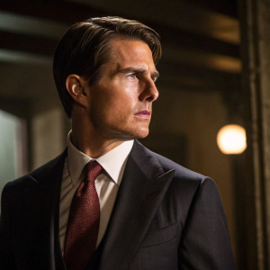 Tom Cruise, actor, dressed in a dark suit with a maroon tie. Intense gaze in a dimly lit room, focusing on his upper body and face.
