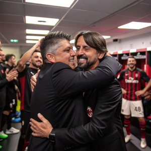 Gennaro Gattuso and Simone Inzaghi embracing post-match. Inside a packed stadium locker room. Dark suits, surrounded by cheering teammates.