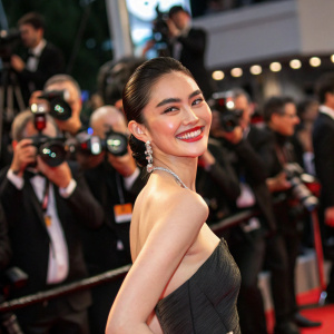 Davika Hoorne, posing with a radiant smile at a glamorous red carpet event. Crowd and photographers in the background.