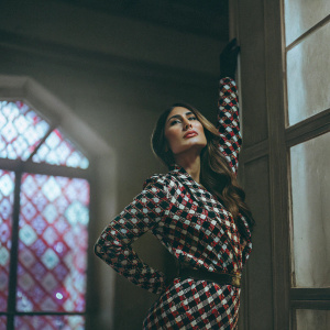 Kareena Kapoor posing confidently. Purple and blue blurred background with bokeh effect. Wearing a chic black and red houndstooth dress.