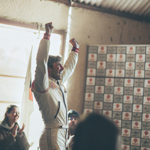 Alvaro Bautista, with a joyful expression, celebrating victory. Wearing a white racing suit with red highlights. The backdrop features numerous sponsor logos. Crowds cheering