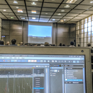 Screenshot of a 3D modeling software interface in Italian. Control panels and tools visible. Tech conference backdrop.