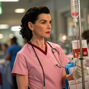 Julianna Margulies as Nurse Carol Hathaway in a bustling city emergency room. Dark hair and serious expression. Pink nurse uniform, examining blood bag amidst medical equipment.