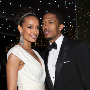 Nick Cannon and Selita Ebanks attend gala event. Selita wears elegant white dress. Nick in black tuxedo. Dark background with sparkling lights