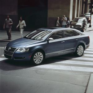 Blue Volkswagen Passat TDI Blue Motion, sleek and polished, parked on a busy street corner. Surrounded by pedestrians and other vehicles.