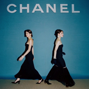 Helena Christensen and Clara McGregor on the CHANEL runway. Black gowns and elegant demeanor. Gray backdrop with massive 'C' logo.