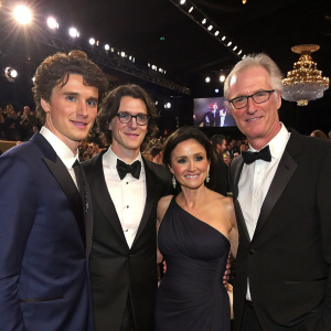 Charles Hall, Henry Hall, Julia Louis-Dreyfus, and Brad Hall, at a glamorous awards ceremony. A crowd of stars in the background.