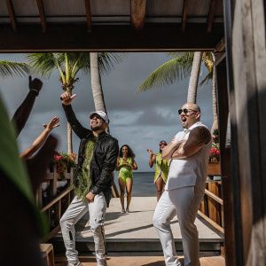 Enrique Iglesias and Pitbull in a vibrant music video scene. Tropical beach backdrop with palm trees. Fun and energetic atmosphere.