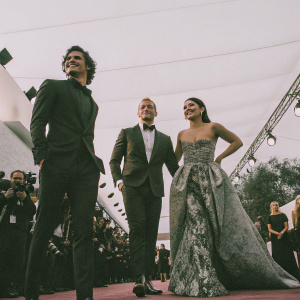 Charles Melton, Alexander Ludwig, and Vanessa Hudgens at a glamorous awards show. Charles Melton, of Hispanic descent, stands tall. Alexander Ludwig, with a muscular build, exudes strength. Vanessa Hudgens beams with joy.