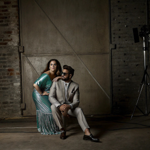 Poonam Dhillon and Riteish Deshmukh at Netflix Films Day. Poonam in teal-green, shiny, striped dress with fringed hemline. Riteish in gray suit. Vibrant pink background.