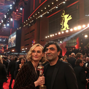 Diane Kruger and Fatih Akin at the Berlinale award ceremony, holding shiny trophies. Crowded indoor event with bright stage lights.