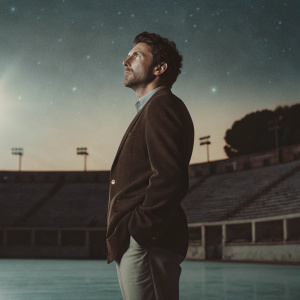 Eusebio Di Francesco, Italian football manager, intense gaze, dark blazer, standing alone on an empty pitch at night. Starlit sky in the background.