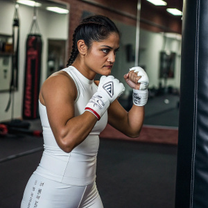Cynthia Calvillo, a UFC fighter, in a sleek white boxing outfit with her signature gloves, posing with fierce determination at a gym.