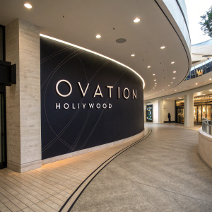 Photograph of Hollywood & Highland shopping center rebranding to Ovation Hollywood. Curved wall with white text on black backdrop. Subtle architectural design and soft lighting
