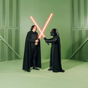 Kylo Ren and Darth Vader in a starkly illuminated room. Both wielding their iconic red lightsabers. Bright studio lights highlighting their imposing figures. High-tech backdrop with geometric patterns.