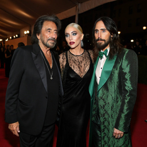 Al Pacino, Lady Gaga, and Jared Leto at the Met Gala. Al Pacino in black suit, Lady Gaga in black velvet gown with lace, Jared Leto in green tuxedo. Dimly lit, red carpet event.