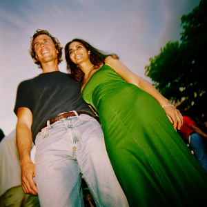 Close-up photo of Matthew McConaughey and Camila Alves at premiere event. Matthew in casual jeans and black t-shirt. Camila in vibrant green dress. Both looking towards camera, background blurred.