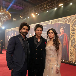 Shah Rukh Khan alongside Saahil Prem and Amrit Maghera at a movie premiere. Lavish backdrop with promotional advertisement