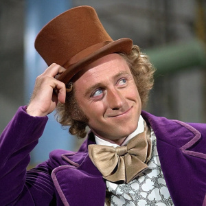 Meme featuring Willy Wonka, the eccentric chocolate factory owner. Purple jacket and brown top hat. Playful pose. Blurred background adds intrigue.