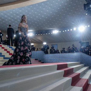 Chiara Ferragni at the Met Gala, wearing an elaborate floral gown and diamond necklace. The venue is crowded with photographers and other celebrities.