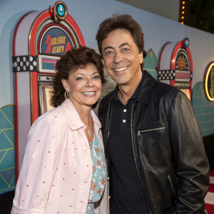 Erin Moran and Scott Baio at a nostalgic 'Happy Days' reunion event, posing with a retro backdrop featuring iconic symbols from the show.