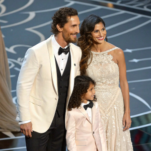 The McConaughey family at an award show. Matthew McConaughey, Camila Alves, Levi Alves McConaughey, Vida Alves McConaughey, and Kay McConaughey. Elegant attire. Joyful expression. On stage with abstract background.
