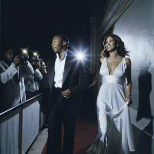 Columbus Short and Aida Abramyan at a gala. Both are elegantly dressed in black and white. Red carpet event with flashing cameras.
