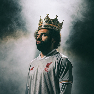 Digital illustration featuring Mohamed Salah, wearing a majestic gold crown over his Liverpool jersey. Dark, smoky backdrop with dramatic lighting.