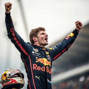 High-resolution image of Max Verstappen in triumphant celebration. Wearing Red Bull Racing's iconic black and gold racing suit. Background blurred. Celebratory pose with intense expression