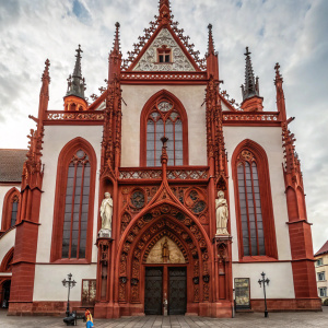 The Marienkapelle, a stunning Gothic cathedral in Würzburg, Germany. Its facade showcases intricate red sandstone pillars and statues of religious figures. The facade features pointed arches and detailed stonework, with rich red and white accents.