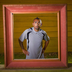 Arturo Vidal, a soccer star, strikes a pose in Nike's latest kit. Gray jersey with black and white details. Standing before a red rectangular frame. Confident expression