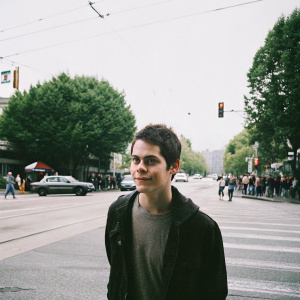 Dylan O'Brien, young actor with short dark hair and freckles, posing for a candid photo shoot in a bustling city street.