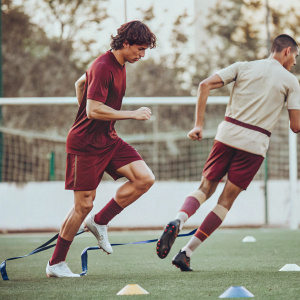 Cristiano Ronaldo and Joao Felix during a vigorous training session at the soccer academy. Green field with fitness gear scattered around.