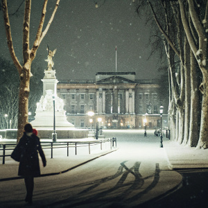A winter scene at Buckingham Palace, UK. Covered in snow, with majestic buildings and statues. Cozy atmosphere.