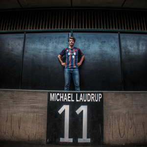 Michael Laudrup, in vintage soccer jersey with '11' number, posed against sleek, modern black backdrop.