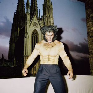 Wolverine, a muscular character, standing in a menacing pose. He has a fierce expression and textured skin. Fantastical setting with dark, gothic architecture.