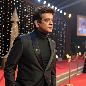 Ravi Kishan, South Asian actor, in a sleek black suit, turtleneck, and stylish hairdo. He is at the Filmfare Awards red carpet. The background is a sparkling stage with awards night ambiance.