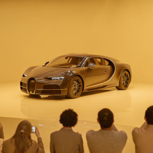 Bugatti Chiron on display at car show. Bright lights illuminate its sleek, glossy body. Spectators gather around.