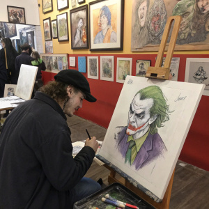 Artist sketching Batman's nemesis, the Joker, in a bustling art studio filled with paintings and sketches.
