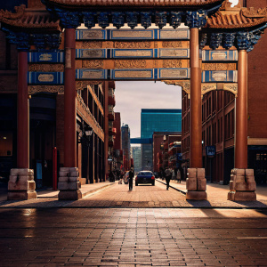 In the heart of Toronto's Chinatown stands a magnificent Chinese-style gateway arch. Its intricate designs and vibrant colors, including gold, red, and blue, dominate the scene. The bustling cityscape serves as a dynamic backdrop.