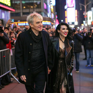 Nick Rhodes and Miss Nefer Suvio, walking down a crowded street filled with fans and paparazzi, vibrant city lights and colorful billboards in the background.