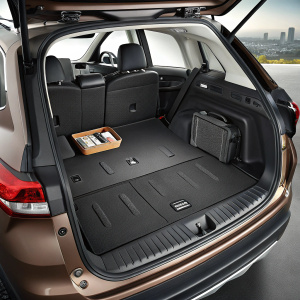 A detailed view of the Nissan Qashqai trunk, showcasing a custom cargo liner for the 2015-2017 models. The dark, smooth panel is seamlessly integrated into the vehicle's design. The open hatch reveals the car's tidy interior, with a few small objects resting on the floor of the cargo area.