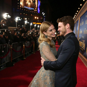 Lily James and Richard Madden, stars of 'Cinderella', hugging at a Hollywood premiere. Crowds and cameras capture the moment on a busy red carpet.