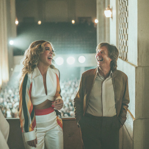 Rita Ora and Paul McCartney sharing a laugh at a crowded concert venue.