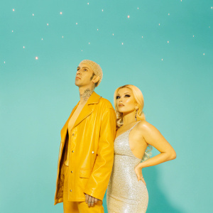 Travis Barker and Shanna Moakler at the MTV Video Music Awards. Travis in a black leather jacket, Shanna in a sparkling silver dress. Both looking glamorous against a dark, starry backdrop.